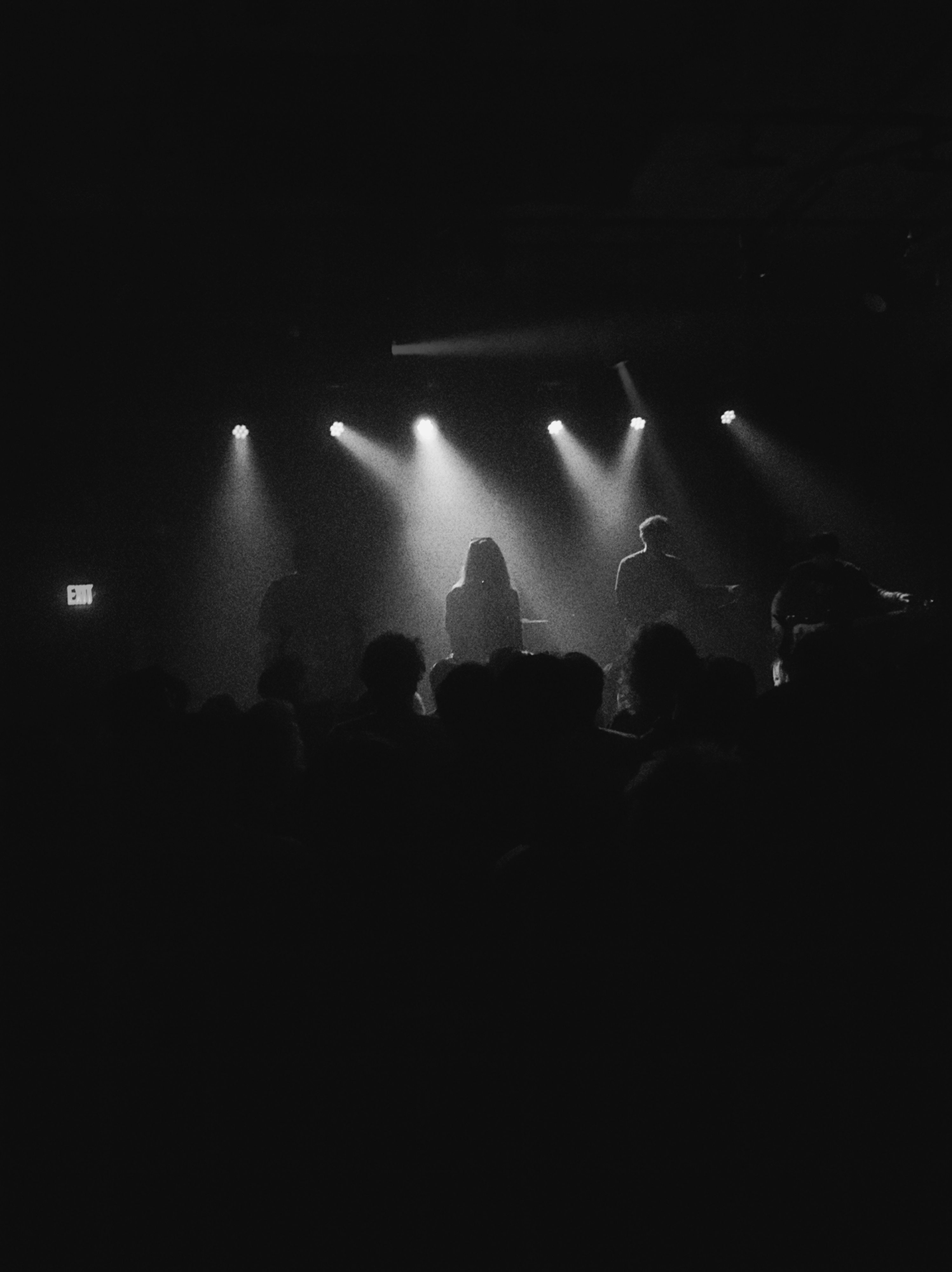 A band on a small stage under a row of spotlights, the crowd below them in silhouette 