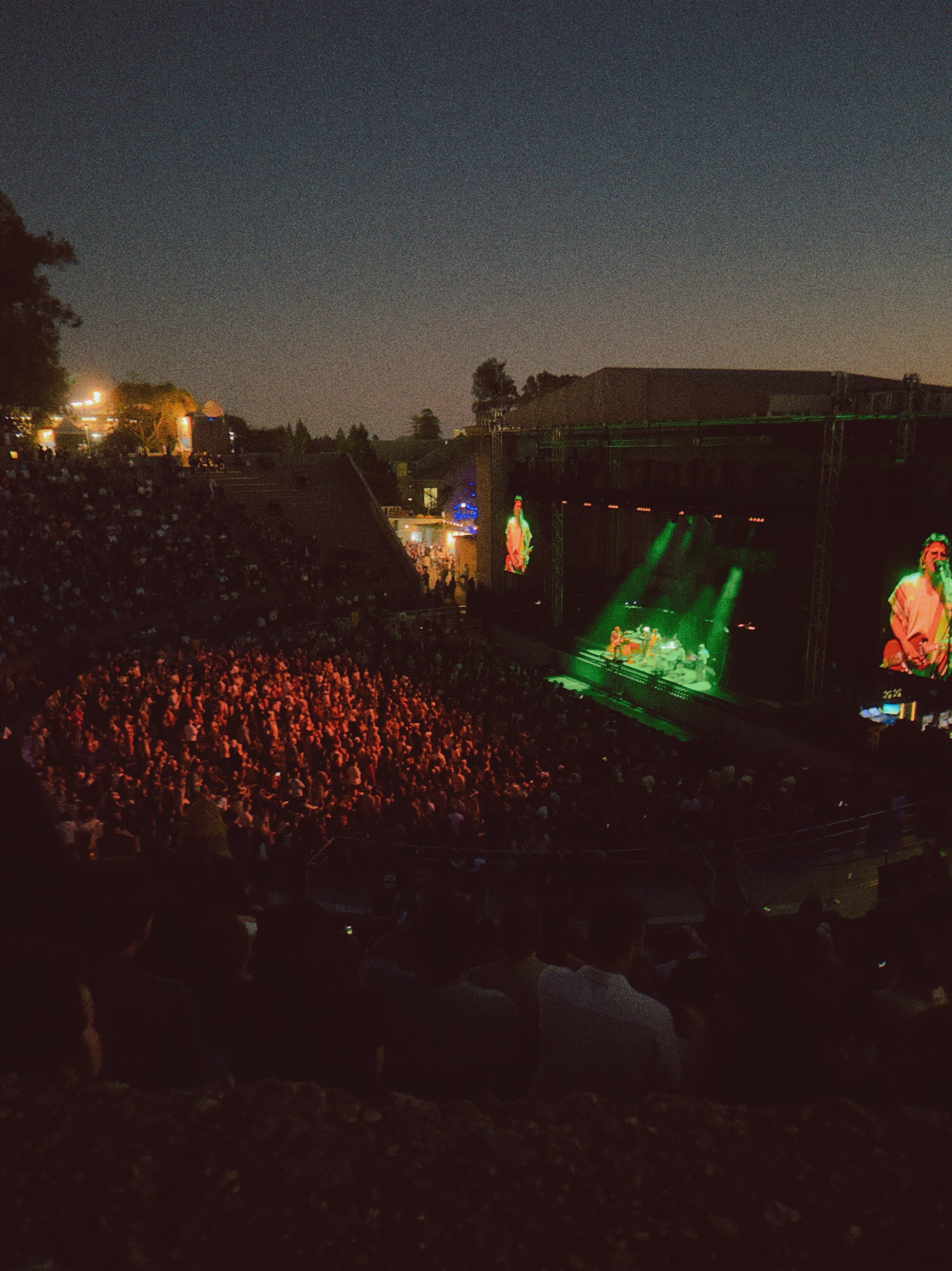 A band opening for a concert at the Greek theater, a crowd below lit in red lights and the band lit in green lights